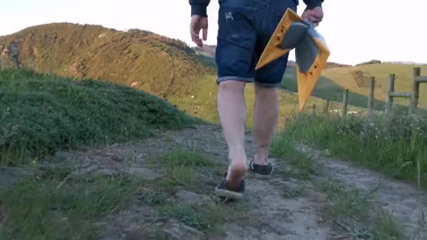 Fiatal férfi hátizsákkal és uszonyokkal a kezében, a part menti ösvényeken sétál. - Felvétel, videó
