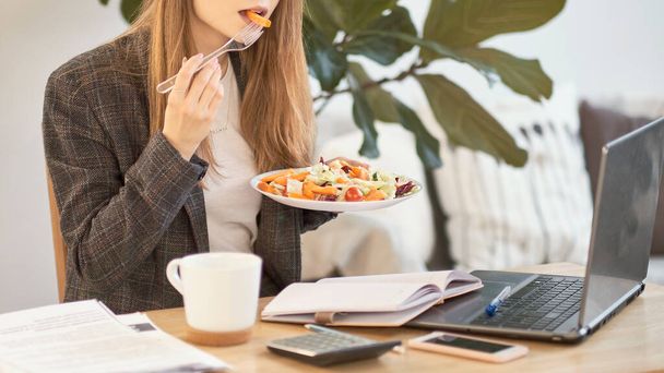Unrecognizable young business woman having a lunch break at desk, she is eating fresh salad, person - Foto, Imagem