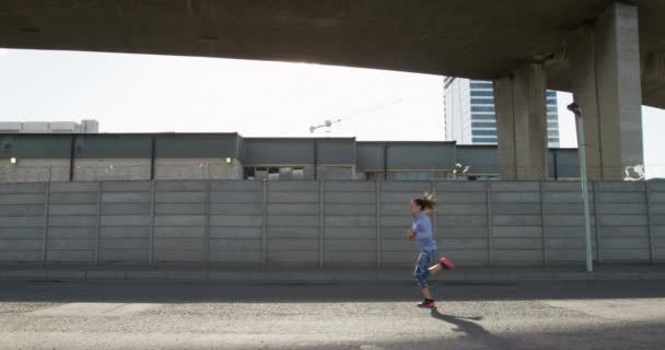 A sporty Caucasian woman with long dark hair exercising on urban area on a sunny day with blue sky, running, in slow motion. - 映像、動画