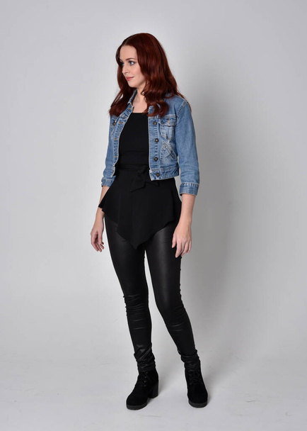  portrait of a pretty girl with red hair wearing black leather pants and denim jacket. Full length standing pose isolated against a  grey studio background - Fotoğraf, Görsel