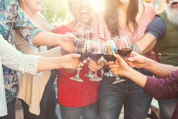 Χαρούμενη οικογενειακή πρόποση με κόκκινα ποτήρια κρασιού στην υπαίθρια τραπεζαρία - Οι άνθρωποι διασκεδάζουν ζητωκραυγάζοντας και πίνοντας ενώ δειπνείτε μαζί - Τρόφιμα και ποτά δραστηριότητες τρόπο ζωής Σαββατοκύριακο - Φωτογραφία, εικόνα
