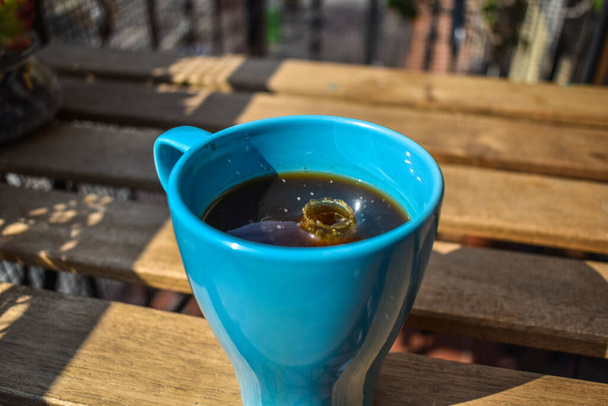 Blue ceramic mug with American coffee and milk drops, splashes, outdoors - Photo, Image