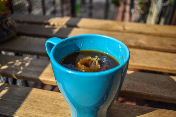 Blauwe keramische mok met Amerikaanse koffie en melk druppels, spatten, buiten - Foto, afbeelding