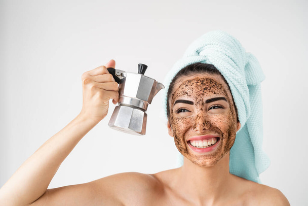 Jovem mulher sorridente aplicando máscara de esfregaço de café no rosto - Menina feliz ter dia de spa de cuidados com a pele saudável em casa - Tratamento de esfoliação natural alternativo e conceito de estilo de vida das pessoas
 - Foto, Imagem