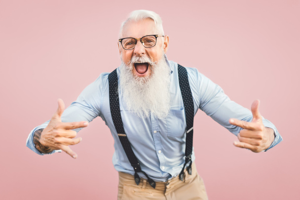 Yaşlı adam kameranın önünde poz verirken eğleniyor - mutlu olgun erkek emeklilikten hoşlanıyor - yaşlılar yaşam tarzı ve hipster kültürü konsepti - pembe arka plan - Fotoğraf, Görsel