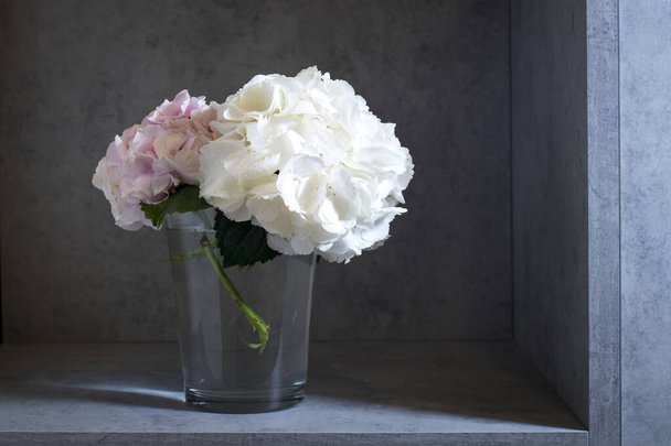 White and pink pastel hydrangea in a glass vase on a gray craft vintage background. Copy space - Φωτογραφία, εικόνα