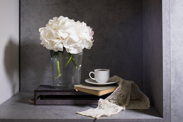 White hydrangea in a glass vase with a small cup of coffee on a book with a notebook. on a gray craft background. - Foto, Imagen