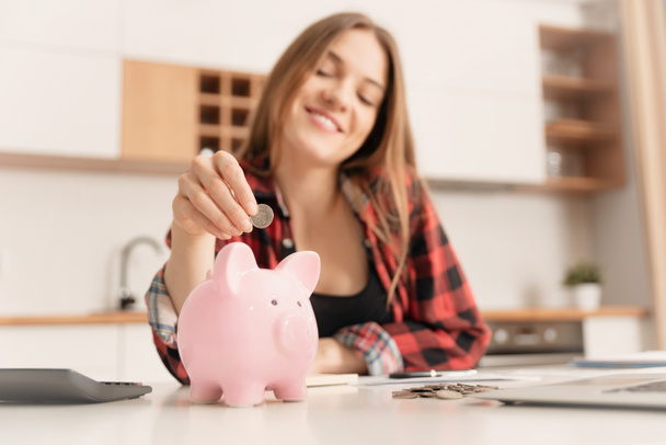 Kadın masadaki domuz kumbarasına para yatırıyor. Ev bütçesi kavramı - Fotoğraf, Görsel