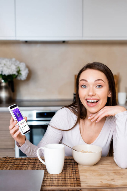 KYIV, UKRAINE - APRIL 29, 2020: excited woman holding smartphone with apple music app near cup and bowl  - Fotoğraf, Görsel