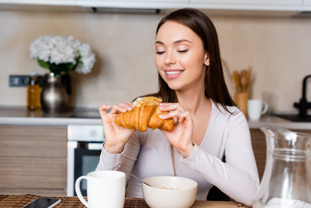boldog lány kezében finom croissant közel tál és csésze  - Fotó, kép