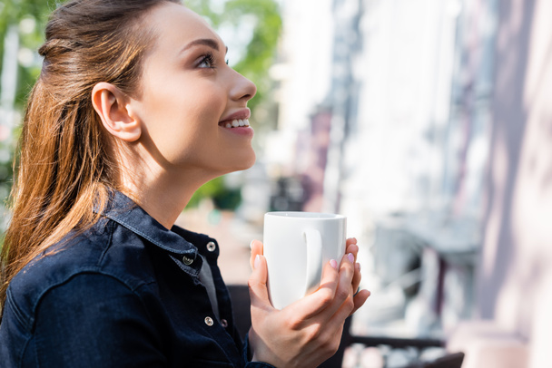 vista lateral de la mujer alegre sosteniendo la taza de café fuera
  - Foto, imagen