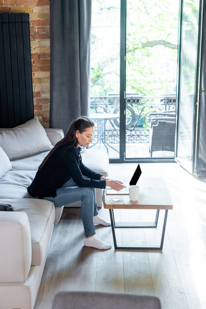 attractive freelancer using laptop with blank screen near cup of coffee on coffee table  - Φωτογραφία, εικόνα