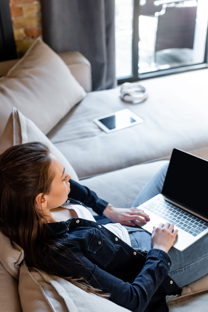 selectieve focus van jonge freelancer met laptop met blanco scherm in de buurt van digitale tablet op bank  - Foto, afbeelding