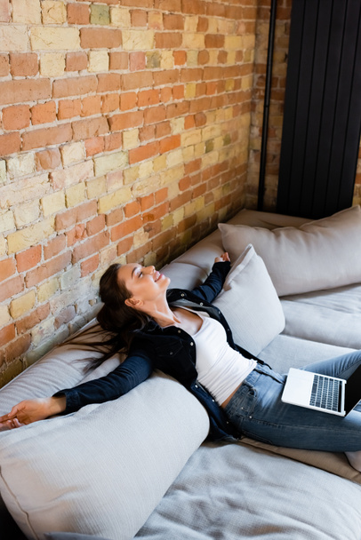 cheerful freelancer with closed eyes relaxing on sofa with laptop  - Foto, imagen