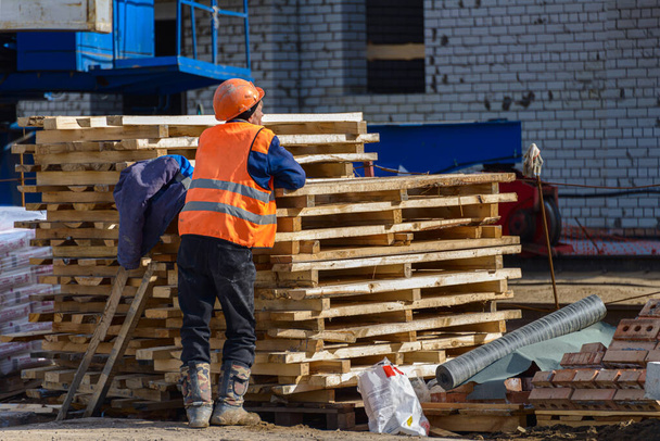Házépítés. Egy munkás egy építés alatt álló új épület építkezésén van. A fapadlók egymásra vannak rakva az építkezésen.. - Fotó, kép