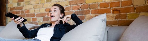 panoramic crop of surprised girl holding remote controller  - Photo, Image