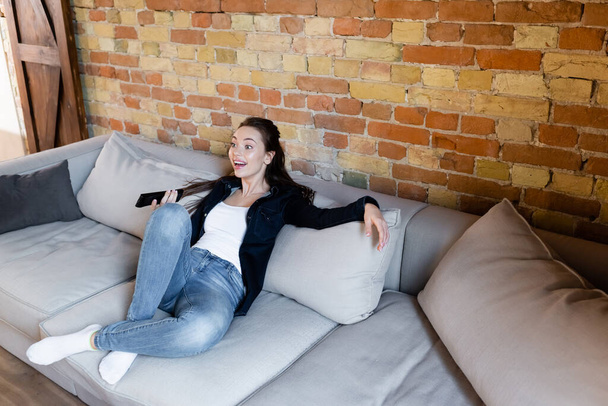excited woman sitting on sofa and watching movie  - Фото, изображение
