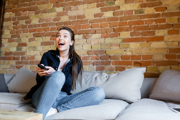 young excited woman sitting on sofa and watching movie  - Foto, Imagem