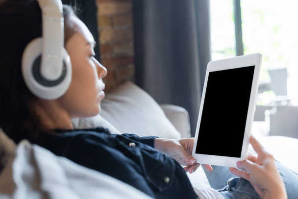 selective focus of girl in wireless headphones listening music and using digital tablet with blank screen - Foto, imagen