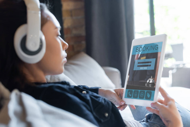 вибірковий фокус дівчини в бездротових навушниках прослуховування музики та використання цифрового планшета з додатком бронювання
  - Фото, зображення
