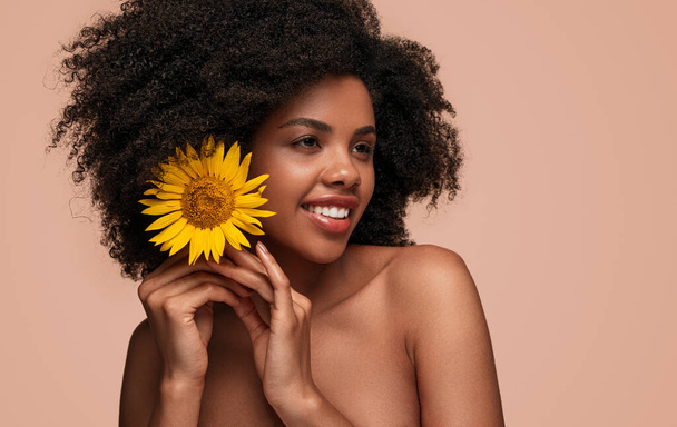 Fröhliche Afroamerikanerin steckt Blume ins Haar - Foto, Bild
