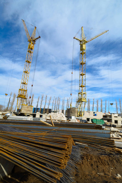 Hausbau. Eisenbeschläge für den Bau eines Neubaus auf einer Baustelle vor dem Hintergrund von Baukränen und blauem Himmel fotografiert. - Foto, Bild