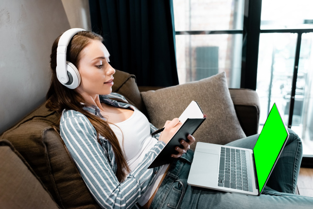 houkutteleva nainen langattomissa kuulokkeissa kirjoittaminen kannettavan tietokoneen lähellä vihreällä näytöllä, online-tutkimuksen käsite
  - Valokuva, kuva