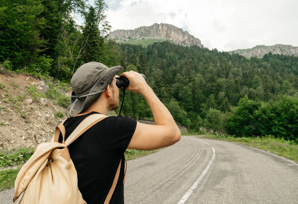 viajero masculino en ropa de senderismo está utilizando binoculares mientras mira los picos de montaña. Viajar y caminar
. - Foto, Imagen