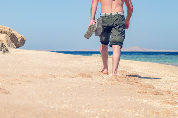 Barefoot man walks along the sandy sea coast. - Фото, изображение