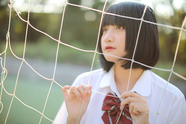 Πορτρέτο της όμορφης ασιατικής ιαπωνικής στολή κορίτσι γυμνασίου ψάχνει με δίχτυ σε πράσινο φόντο - Φωτογραφία, εικόνα