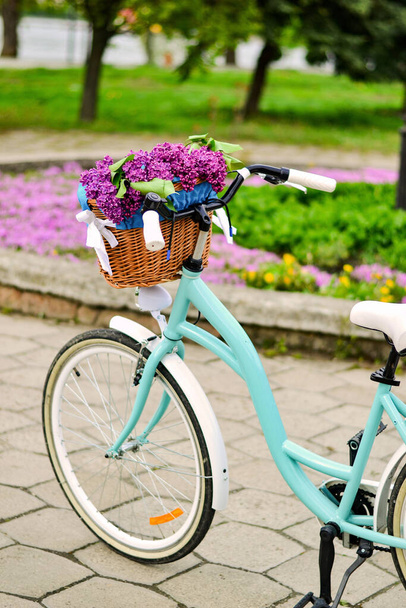 Τυρκουάζ ποδήλατο με καλάθι με λουλούδια. Καλάθι με μωβ πασχαλιά - Φωτογραφία, εικόνα