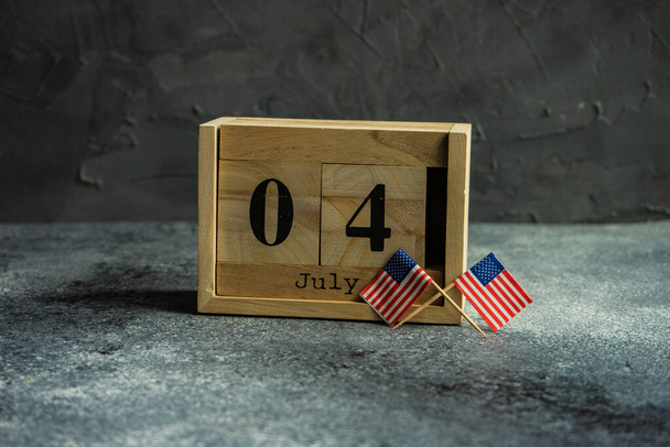 4th July celebration card concept with wooden calendar and USA flags on grey background with copy space - Foto, Imagem