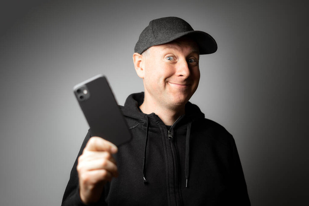 Άντρας με μαύρα ρούχα ευχαριστημένος με το μήνυμα στο τηλέφωνο ή το ίδιο το τηλέφωνο. - Φωτογραφία, εικόνα