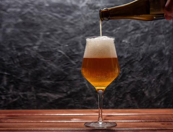 A pint of light beer is poured into a glass of Belgian form from a bottle on a wall in grunge or loft style - Photo, image