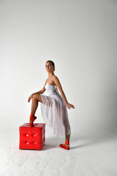 ballerina in a white dress and red pointe shoes and a white chair on a white background - Fotoğraf, Görsel