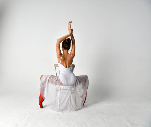 balerina egy fehér ruha és piros pointe cipő és egy fehér szék fehér háttér - Fotó, kép