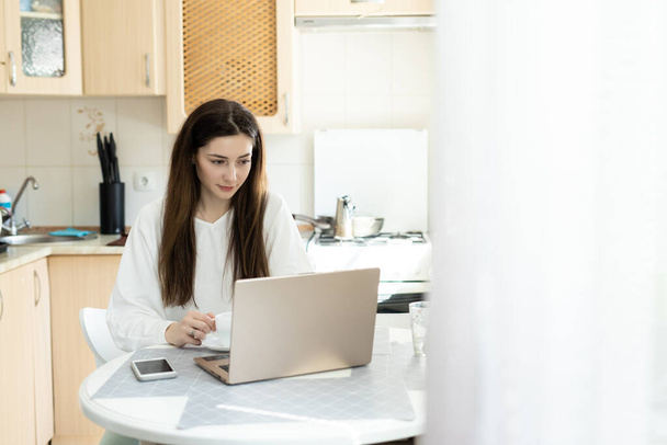 La chica tachonado en línea con el ordenador portátil en la cocina. El estudiante estudia en línea y el aprendizaje de nuevas asignaturas con el profesor virtual. Concepto de aprendizaje electrónico a distancia
 - Foto, Imagen