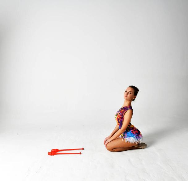 гімнастка в яскравому костюмі танцює з червоними клубами
 - Фото, зображення