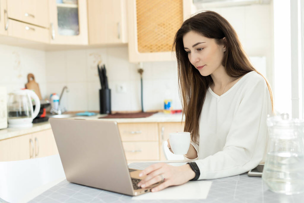 Молодий студент електронного навчання з ноутбуком і пити каву на кухні вдома. Студент вивчає онлайн та вивчає нові предмети з віртуальним вчителем. Концепція електронної освіти
 - Фото, зображення