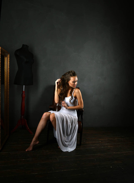 ballerina in a white dress and red pointes sits in a brown chair on a gray background - Photo, Image