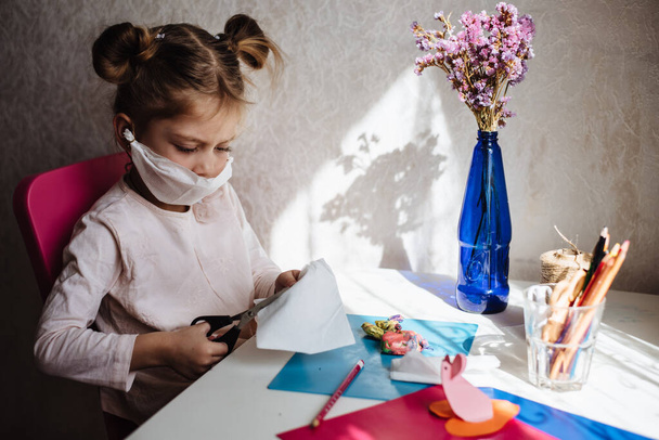 Пятилетняя девочка в медицинской маске занимается творчеством. Защитная маска своими руками. Что делать, чтобы изолировать ребенка. Обучение на дому во время карантина. Домашние развлечения
. - Фото, изображение
