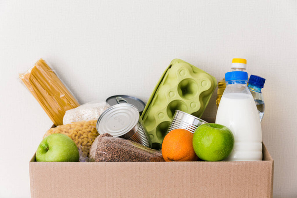 Charity donation box made of cardboard with food with oil, milk and water, herbs, apples and oranges, cereals and canned food, rice and pasta. White background. Close up - Foto, imagen