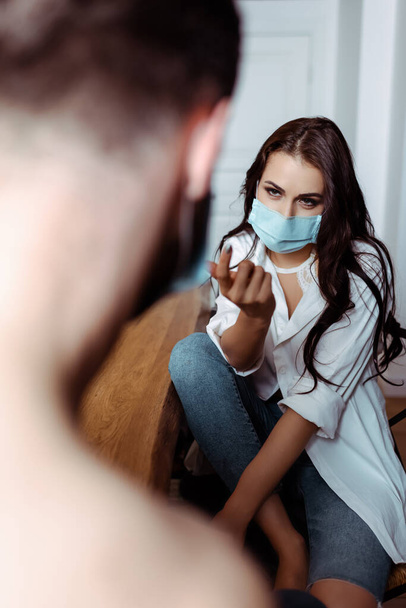 selective focus of sexy young woman in medical mask attracting boyfriend in kitchen - Fotó, kép