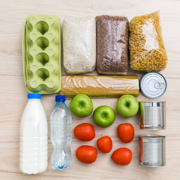 Charity donation food set with oil, milk and water, herbs, apples and oranges, cereals and canned food, rice and pasta. Wooden kitchen table background in Scandinavian interior. Flatlay, top view - Fotó, kép
