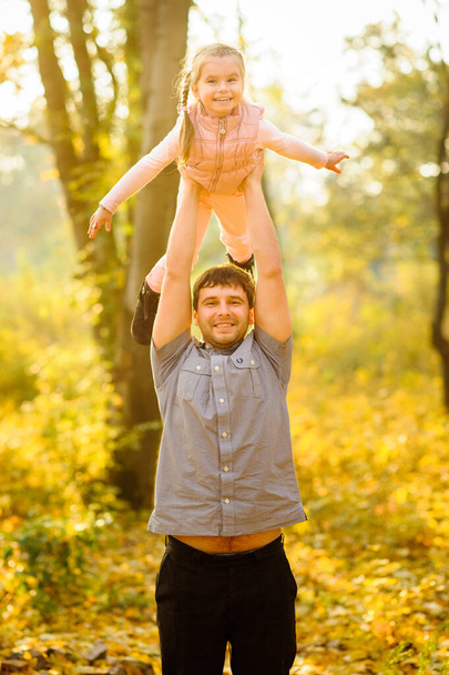 Vader en dochter hebben plezier samen. Papa houdt zijn dochter boven zijn hoofd.. - Foto, afbeelding
