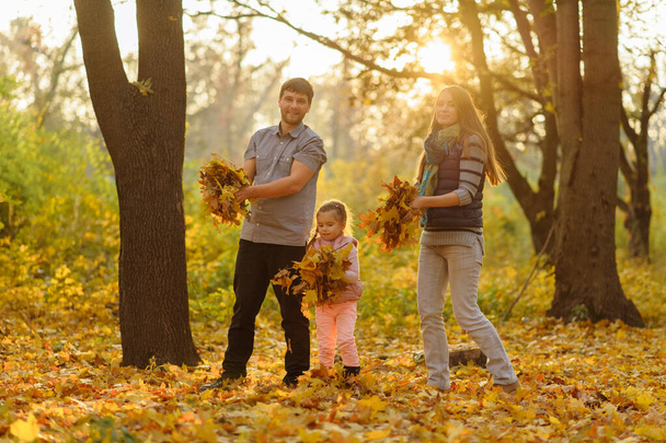 Padre mamá y su hija arrojan hojas de otoño al cielo
. - Foto, imagen