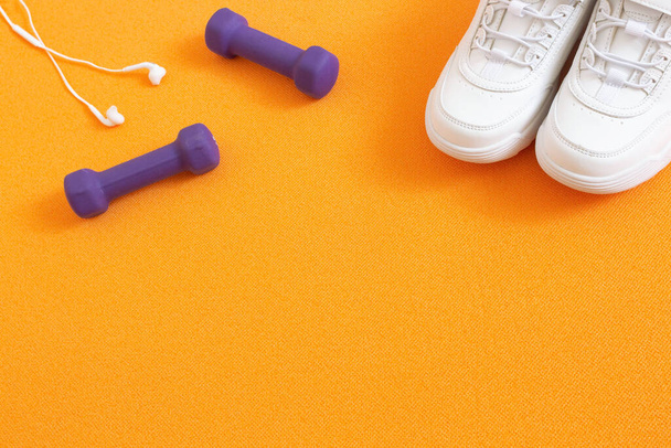 Sneakers, manubri e cuffie sullo sfondo del tappeto fitness arancione. Composizione laica piatta. Concetto di sport, fitness, stile di vita sano. Vista dall'alto. Copia spazio
. - Foto, immagini
