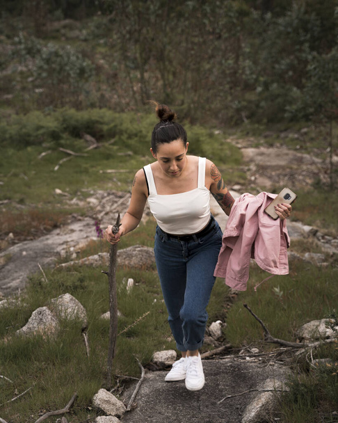 young woman doing trekking in the bush with modern clothes, tattoos and connected - Photo, Image