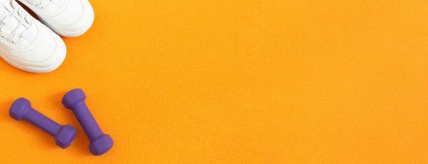 Sneakers e manubri sullo sfondo di un tappeto fitness arancione. Composizione laica piatta. Concetto di sport, fitness, stile di vita sano. Vista dall'alto. Ricevuto. Bandiera
 - Foto, immagini