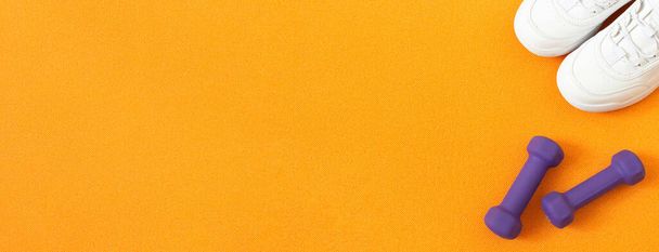 Turnschuhe und Kurzhanteln auf orangefarbener Fitnessmatte. Flache Lagekomposition. Konzept von Sport, Fitness, gesundem Lebensstil. Ansicht von oben. Kopierraum. Banner - Foto, Bild